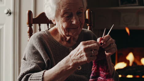 elderly woman knitting by the fireplace