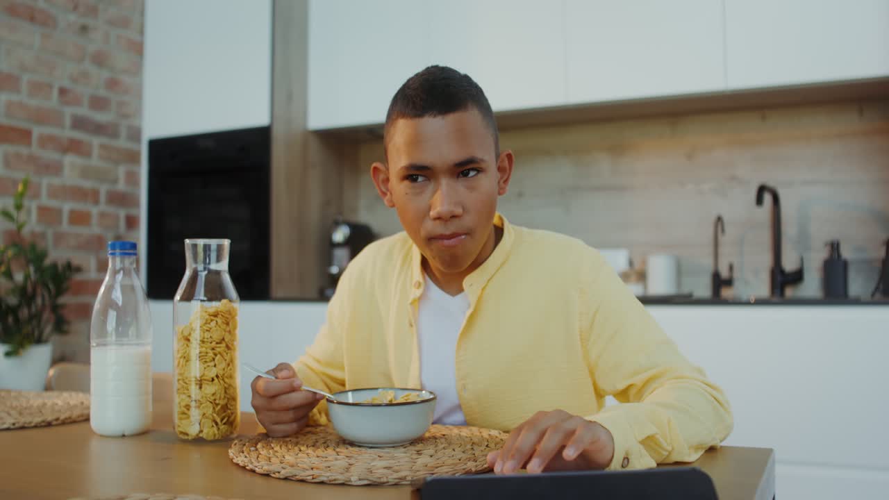 adolescente desayunando y usando una tableta en una cocina