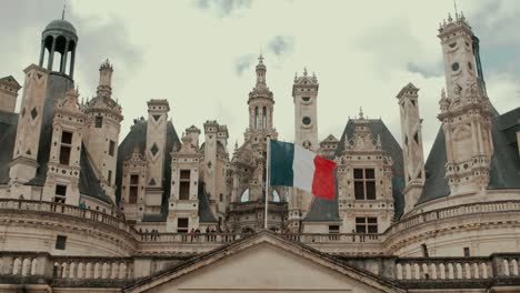 low angle static view of chambord castle facade with french flag waving in cloudy day