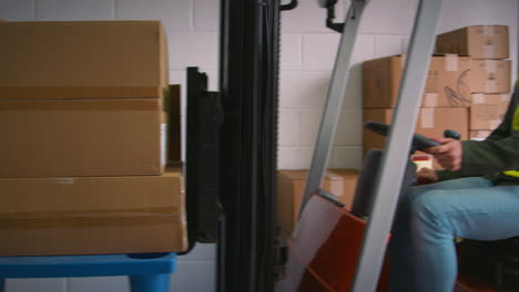 female worker with clipboard in warehouse talking to colleague driving fork lift truck