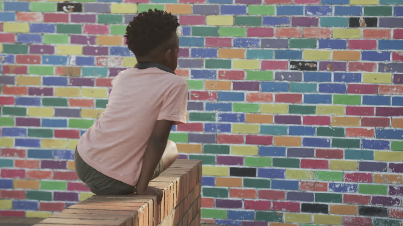 Sitting on brick wall, African American boy looking at colorful mural in schoolyard