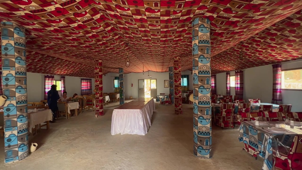 Cameriere berbero che serve i turisti in un colorato ristorante berbero tradizionale con decorazioni rosse e blu, Tunisia