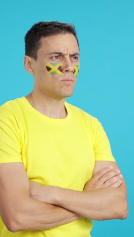 Man with jamaican flag painted looking away with serious expression