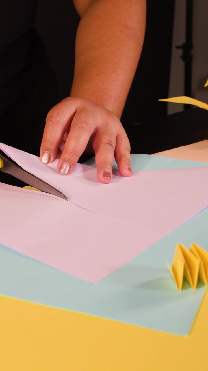Persona che taglia carta rosa con le forbici su una scrivania colorata