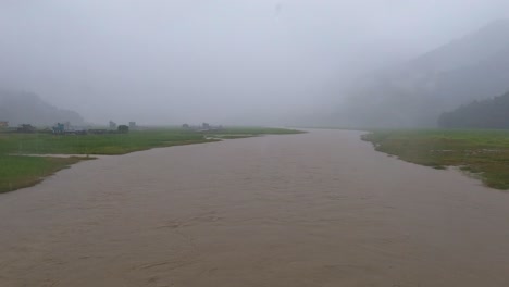 parado en un puente bajo una fuerte lluvia mirando el río inundado durante el monzón en nepal