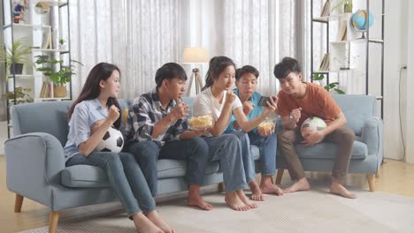 asian teenagers cheering and watching football game on smart phone at home