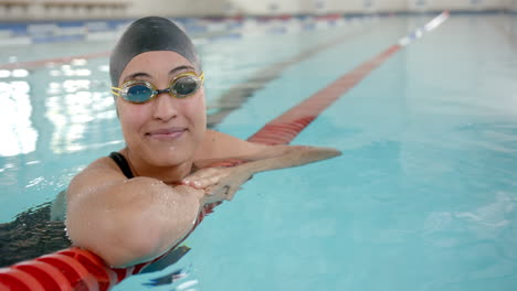 smiling female swimmer resting at pool edge, wearing swim cap and goggles, copy space