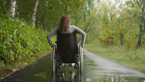 young woman in wheelchair after injury walks in park in rain