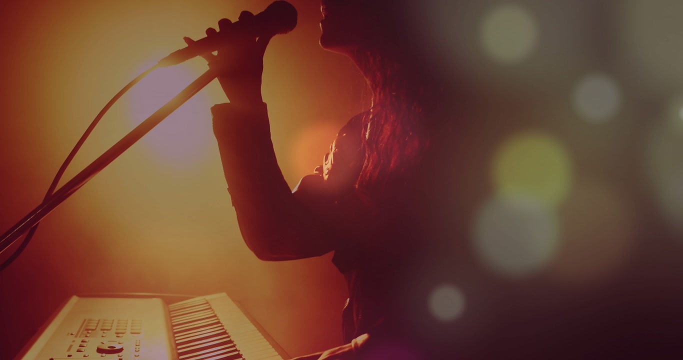 Musician playing keys, reaching mic and singing, bokeh glowing around silhouette for music