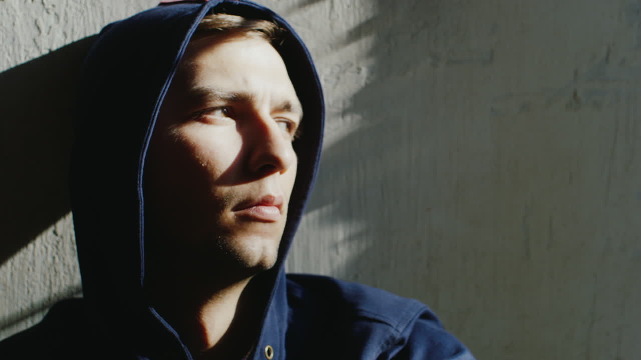 molesto joven encapuchado sentado cerca de una ventana