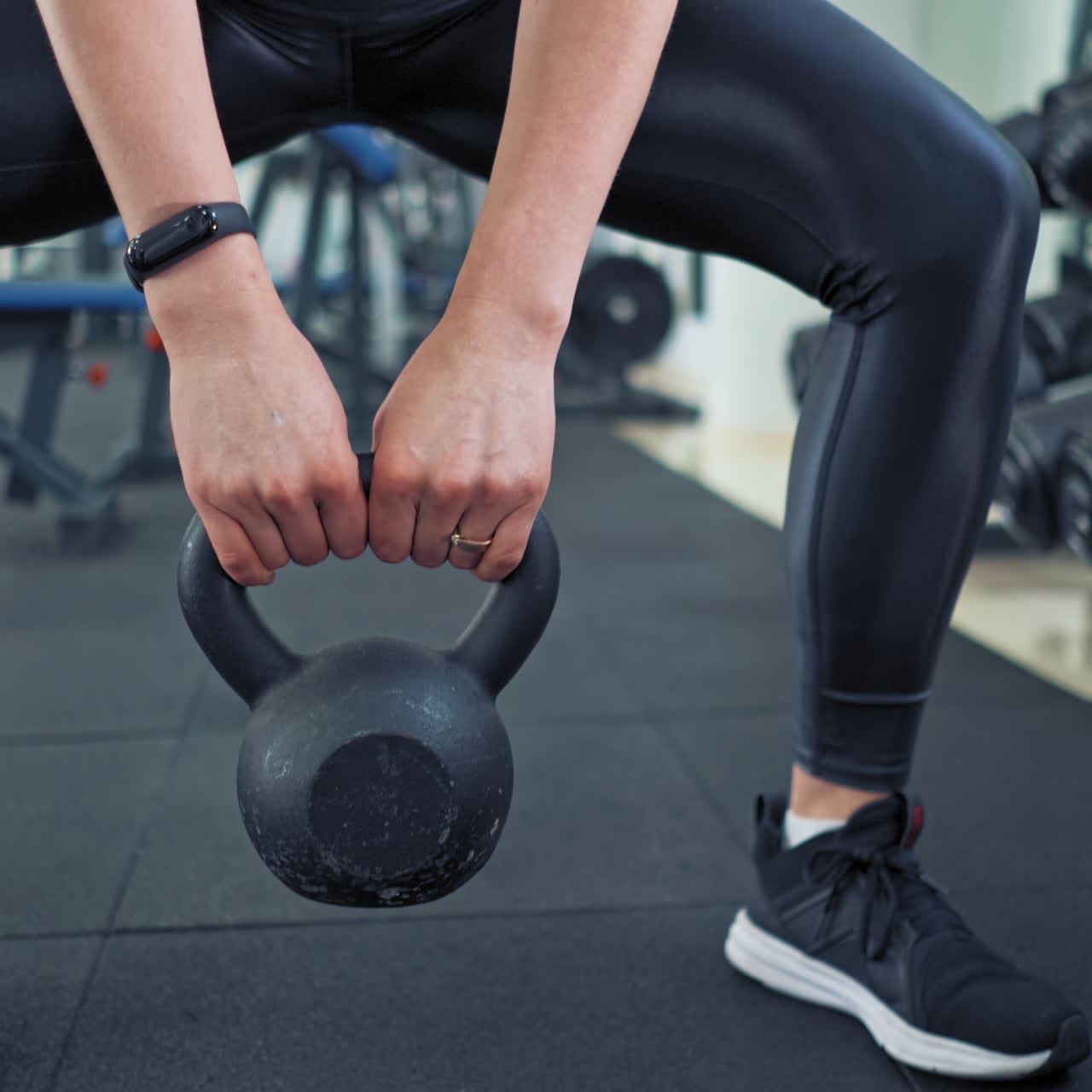 Sporty female lifting kettlebell. Athlete woman wearing black leggings and trainers training with hard weight in sports club. Close-up.