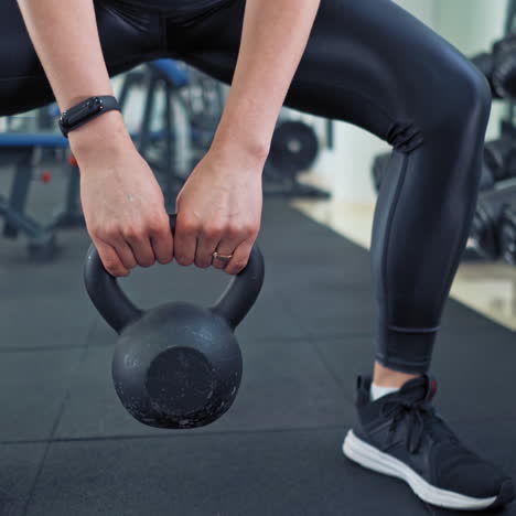 sporty female lifting kettlebell. athlete woman wearing black leggings and trainers training with hard weight in sports club. close-up.