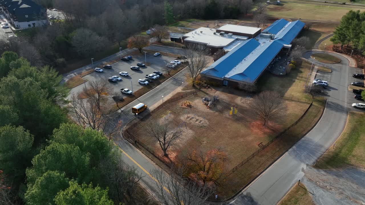 American yellow school bus waiting for pupils of elementary school on sunny autumn day. Aerial approaching shot. Virginia, USA in fall season. School scene with playground