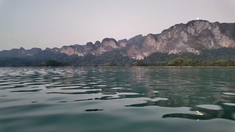 Panning-clip-showing-traditional-wooden-boat-moving-over-shallow-water-surrounded-by-beautiful-mountain-and-forest-landscape