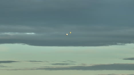 Vista-Lejana-De-Dos-Globos-Aerostáticos-Que-Vuelan-Contra-El-Cielo-Nublado-Al-Atardecer