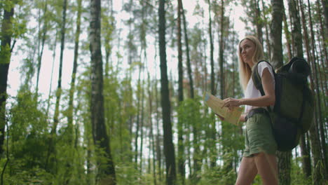 a young woman with a map walks through the forest traveling with a backpack in slow motion