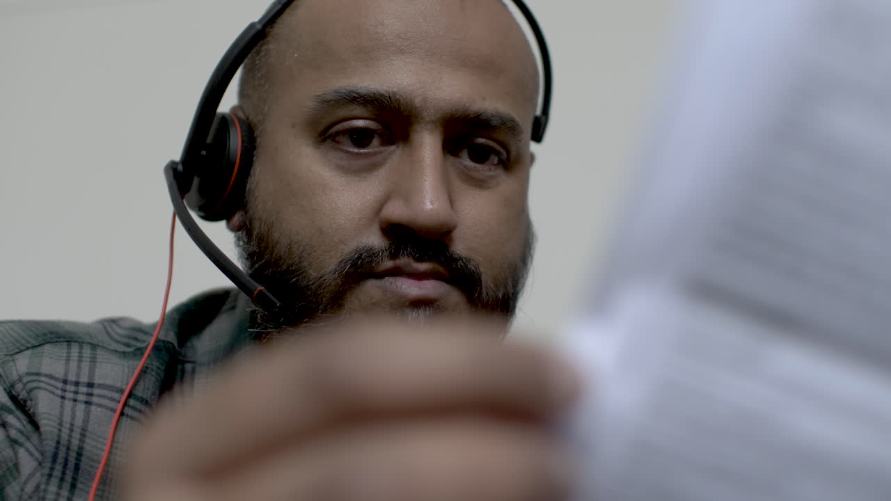 reino unido hombre asiático usando auriculares trabajando desde casa abatido mirando facturas