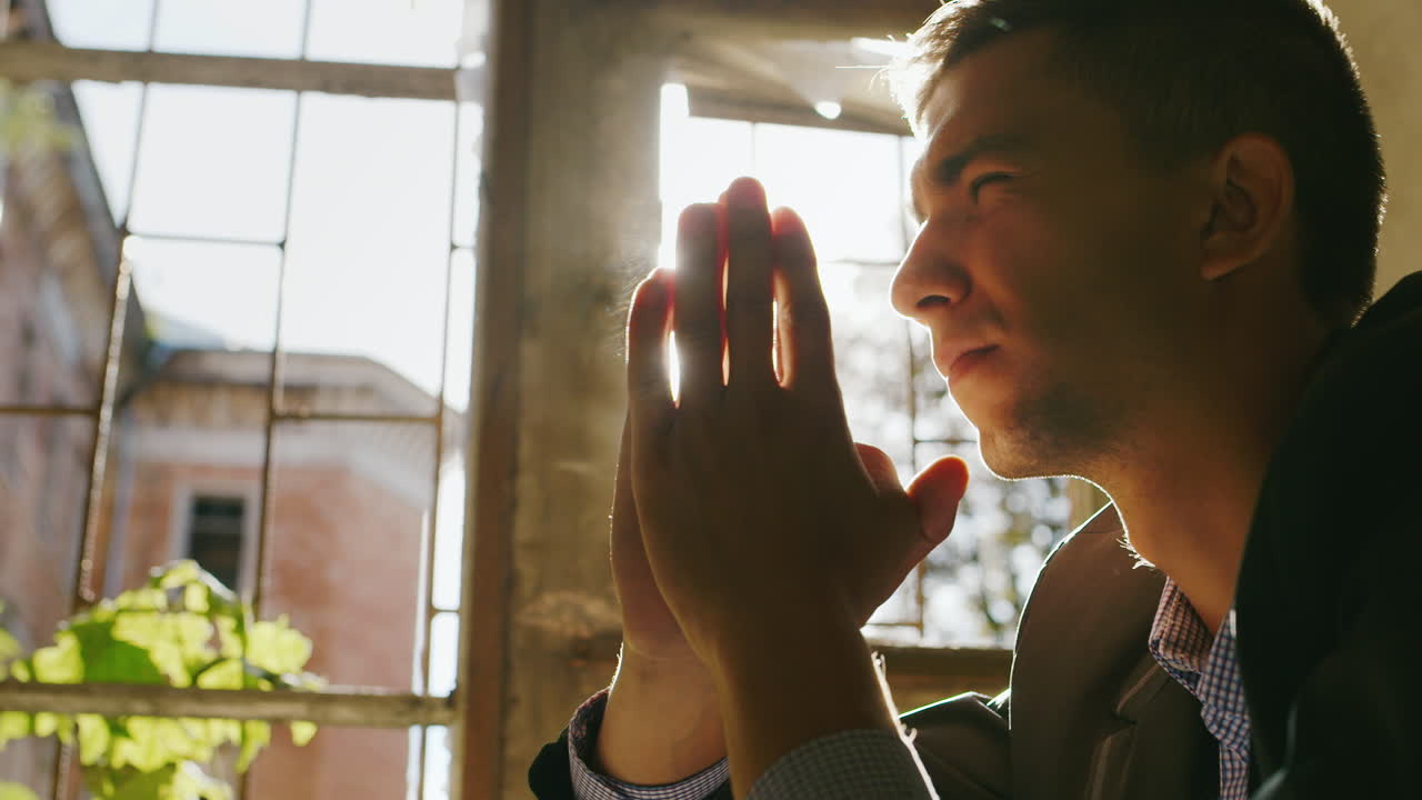 오래된 건물의 창가에 앉아 태양 아래에서 기도하는 젊은 남자의 초상화