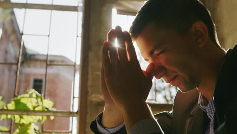 portrait of a young man praying in the sun sitting by the window in an old building