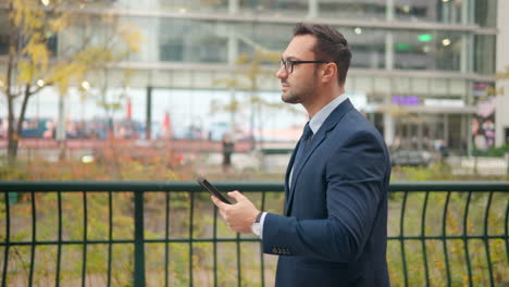 Un-Hombre-De-Negocios-Ocupado-Usando-Un-Teléfono-Móvil-Al-Aire-Libre,-Un-Hombre-Caminando-Con-Un-Teléfono-Inteligente-En-La-Calle-De-La-Ciudad---Vista-Lateral-De-Seguimiento