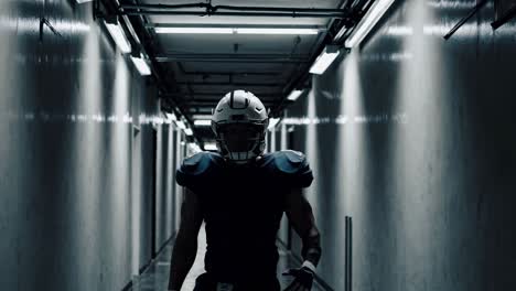 jugador de fútbol americano caminando por un corredor de hormigón débilmente iluminado, con uniforme y casco, encarnando determinación e intensidad atlética antes del tiempo de juego