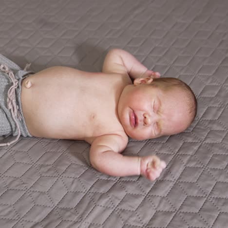 lovely baby on the bed wearing pants only. cute baby lying on the broad bed and sneezing. infant kid on the grey backdrop view from above
