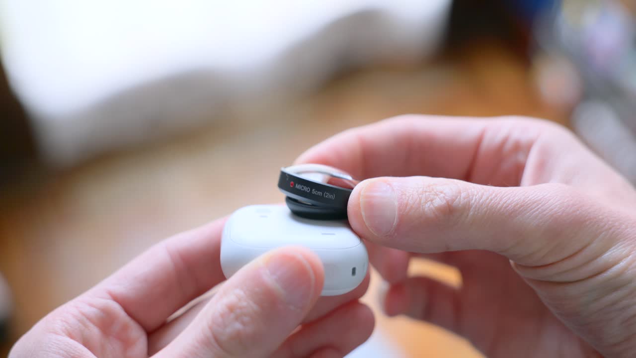 Close-up of hands attaching magnetic ND filter to lens of small white action camera like Insta360 Go