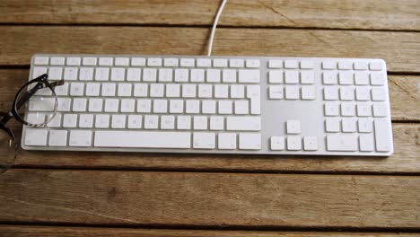 spectacles and keyboard on wooden table 4k