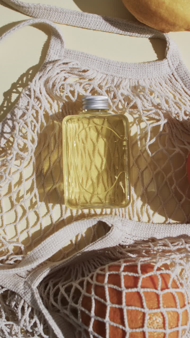 Vertical video of net bag with beauty product bottle, citrus and copy space on yellow background