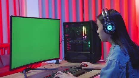 young asian girl gamer playing video game with green screen monitor