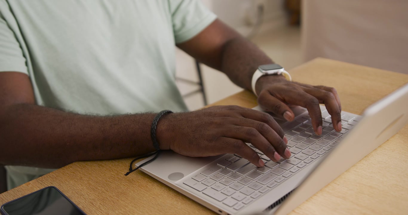 Volwassen Afrikaanse man legt handen op laptoptoetsenbord, typt en werkt aan een houten tafel
