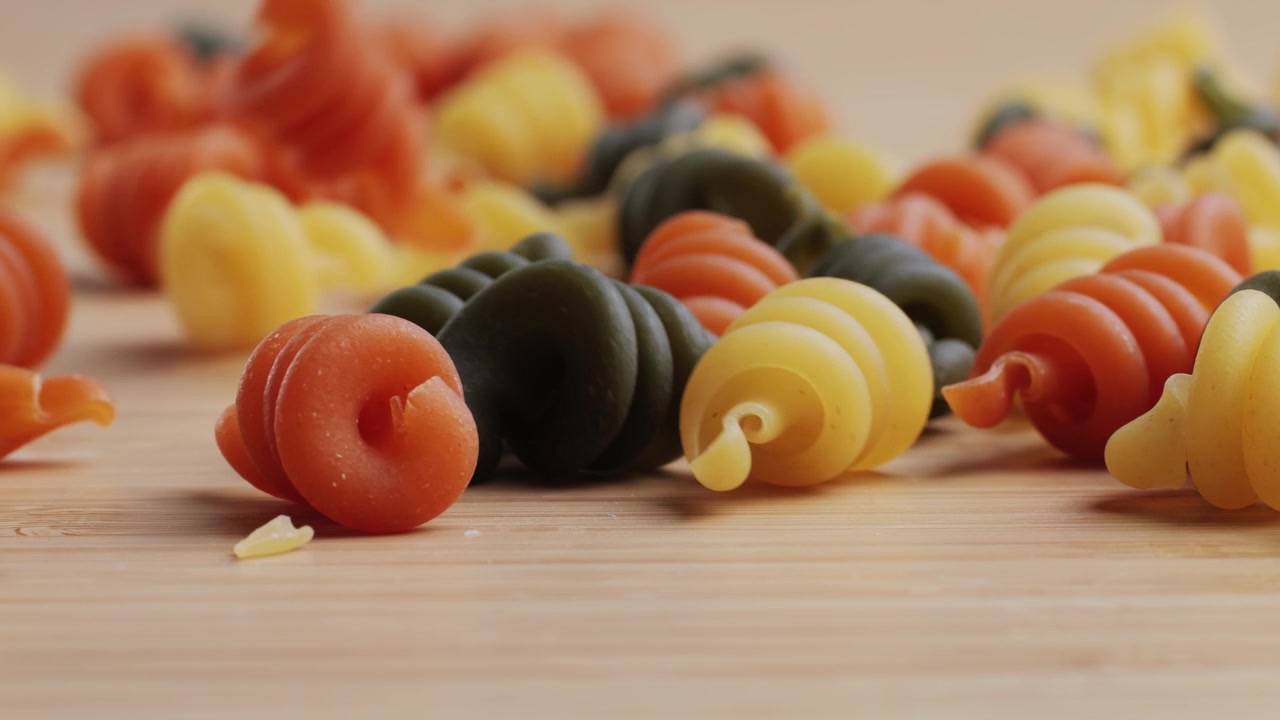 Colorful Spiral Pasta Falling onto a Wooden Surface in Slow Motion