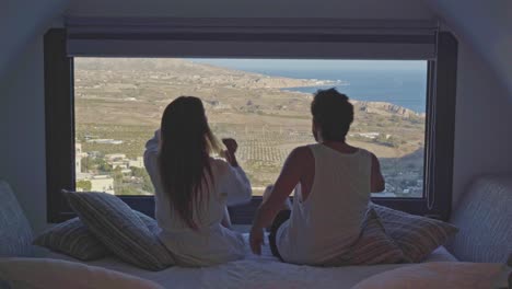 young man walks room with beautiful view, woman leans into him as a romantic gesture