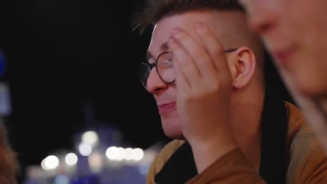 young man wearing glasses chatting at night in outdoor social setting