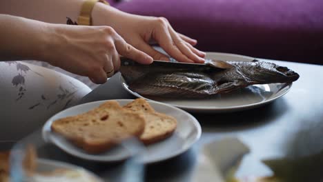 smoked fish meal with bread for breakfast, female hands cutting fish