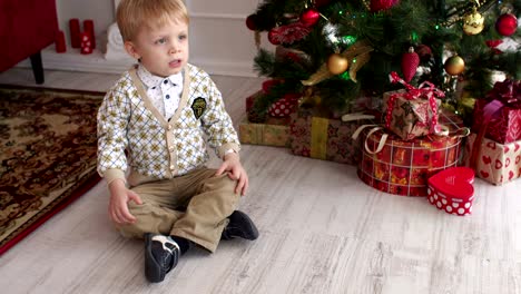 child is sitting near the christmas tree and yawns