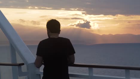 young man on a ship looking the ocean at sunset