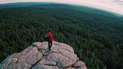 hiker on mountain cliff overlooking pine forest