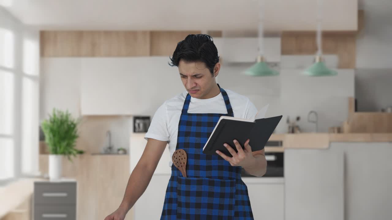 cocinero indio confuso haciendo comida a partir de un libro de recetas