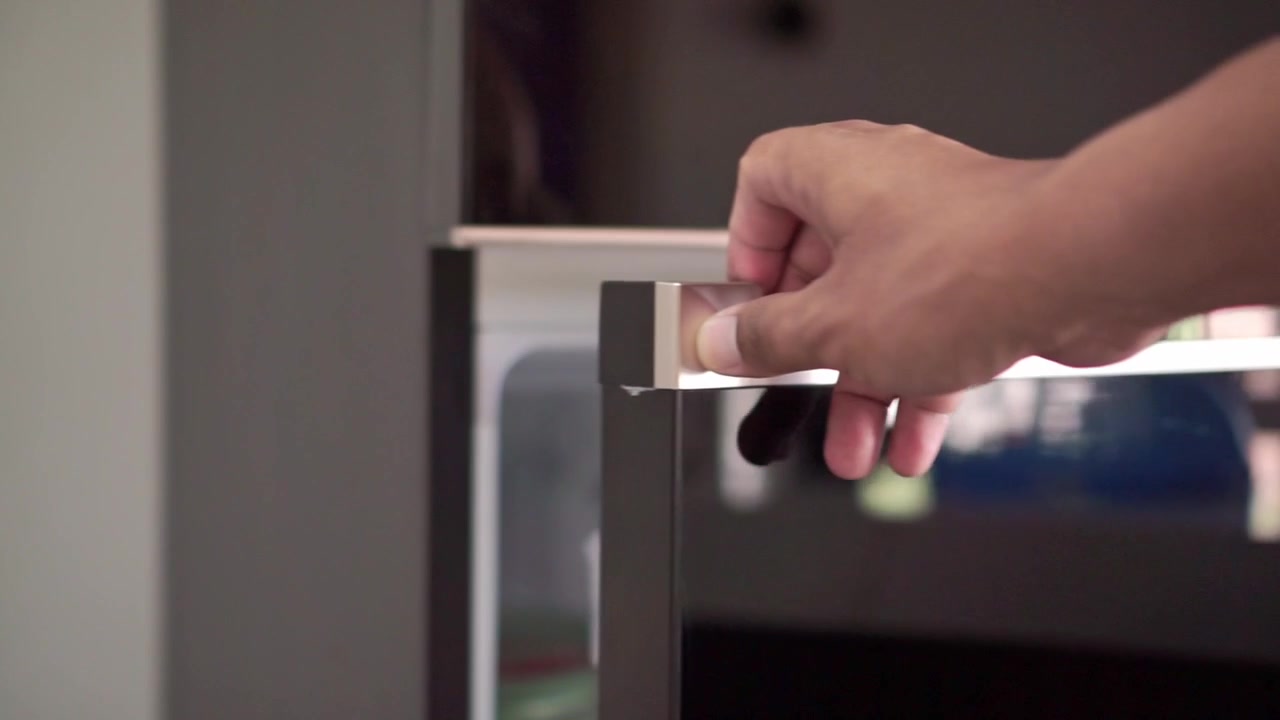 Mano agarrando el tirador de la puerta del frigorífico y abriéndola. Concepto de rutina de cocina y electrodoméstico