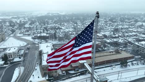 aerial close up of american flag waving over snowy suburban landscape