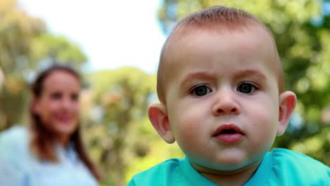 lindo bebé sentado en la hierba con la madre detrás de él
