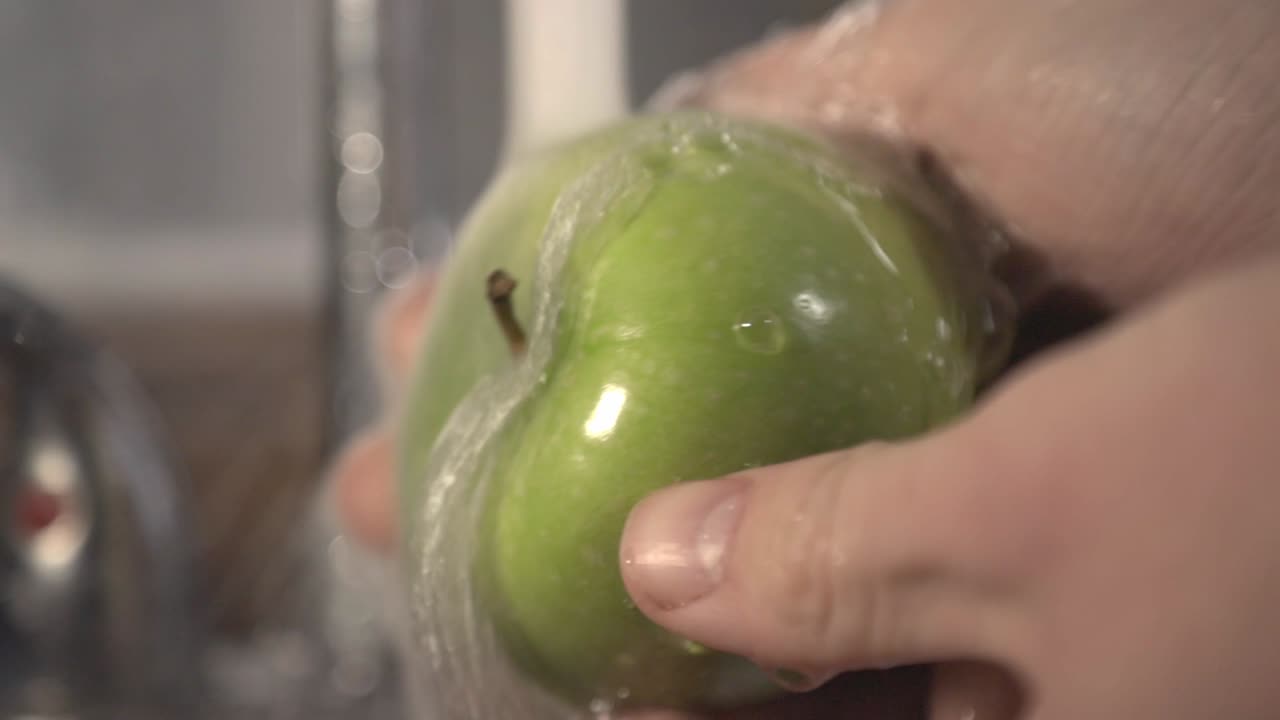 Cleansing The Green Apple With The Running Water From The Faucet. -close up shot