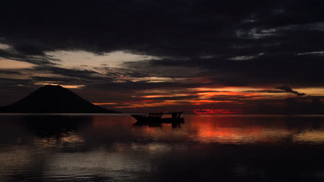 a silhouette of a small boat and a volcano during a fiery sky sunset