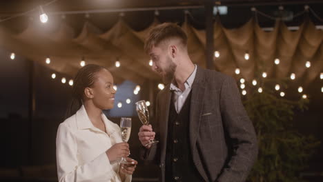 man and woman toasting with champagne glasses while taking a selfie video at new year's eve party