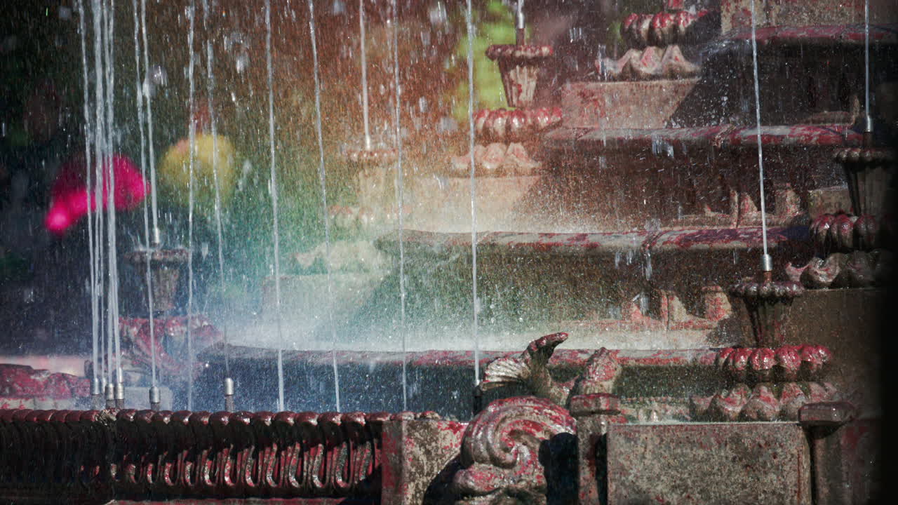View of a decorative fountain with sparkling water droplets illuminated by sunlight in a park