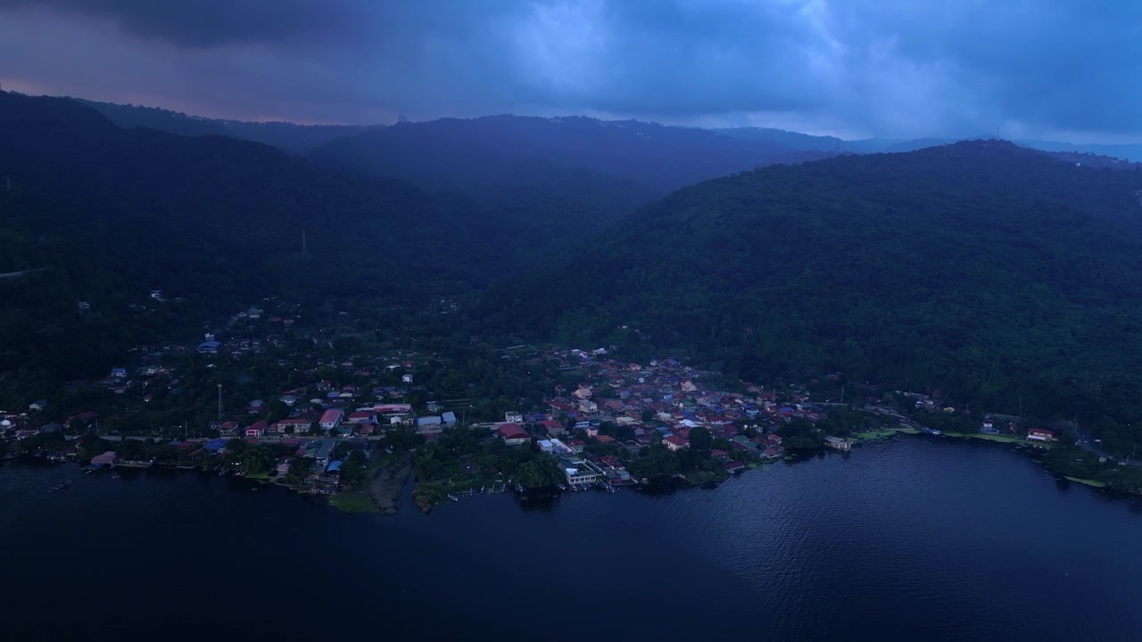Riprese aeree ad alta quota che mostrano l'acquacoltura d'acqua dolce, un vasto paesaggio lacustre, terreno montuoso e sviluppi residenziali che circondano il Lago Taal durante l'ora blu
