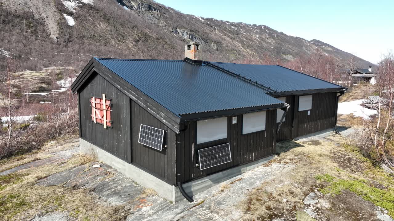 cerrada pequeña cabaña de montaña tradicional en noruega montaña - día soleado de primavera con panel solar en la pared y fondo de la montaña