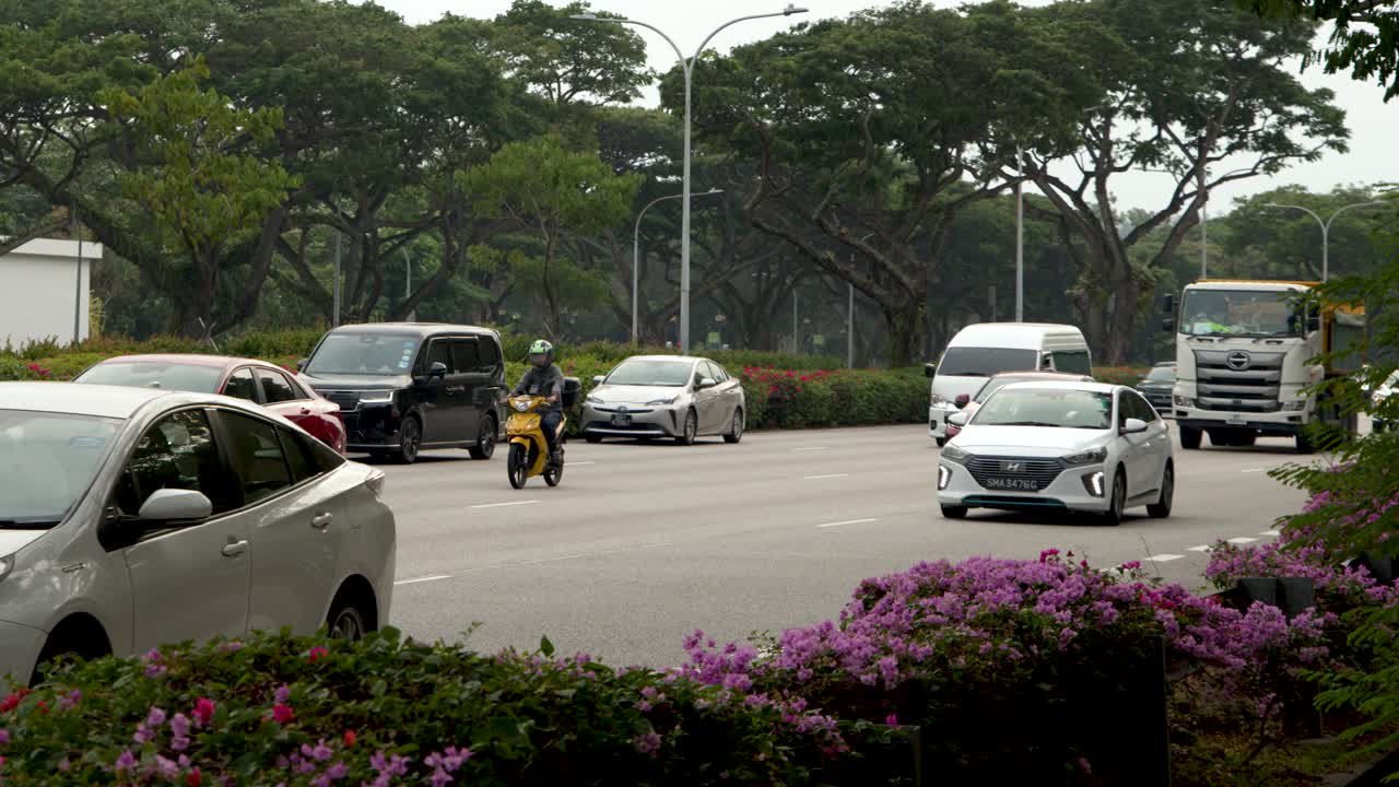 Kendaraan termasuk mobil, truk, dan sepeda motor berlalu lalang di sepanjang jalan tropis yang lebar pada siang hari
