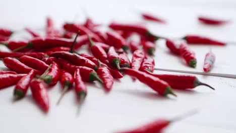 multiple red chili peppers falling and bouncing at white wooden table in slow motion